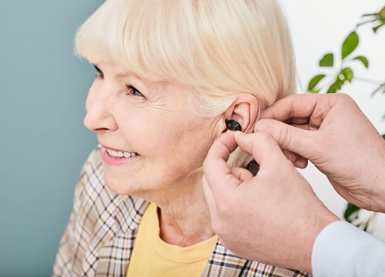 Smiling senior woman being fitted with a hearing aid.