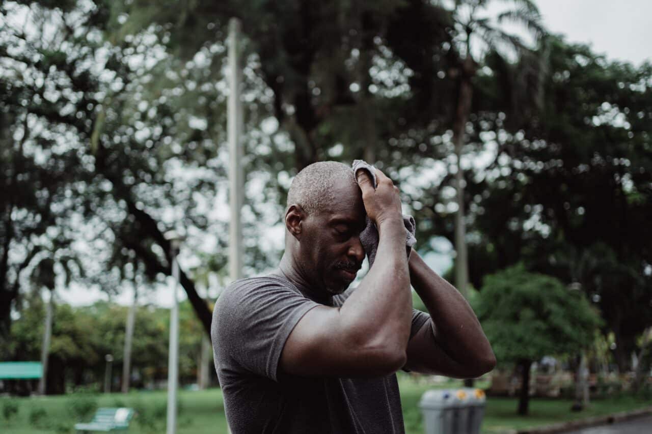 Senior man wiping sweat off his brow after working out on a hot day.