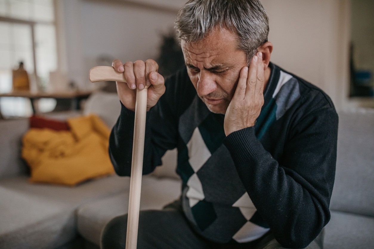 Man sitting on the couch with a cane holding his ear